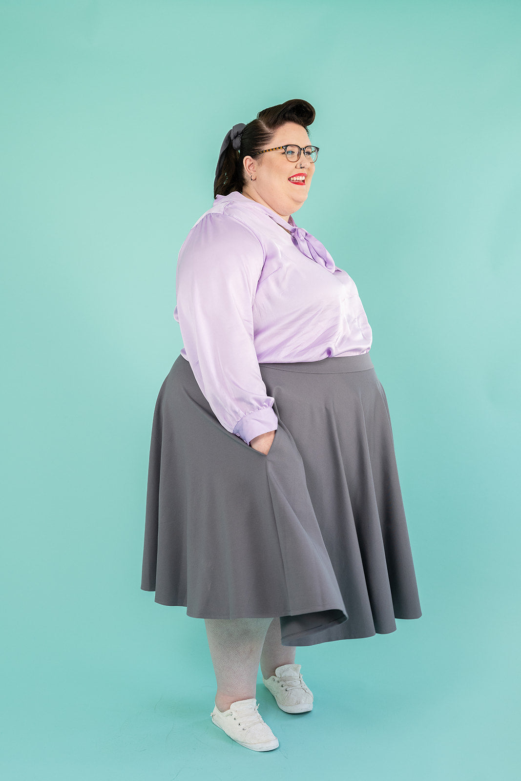 Photo of plus-size brunette woman in lilac coloured blouse and grey skirt