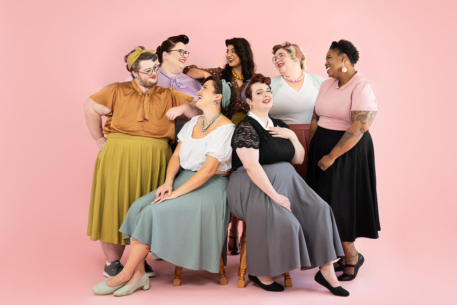 A group of femme-presenting people are posed in a group; they are all wearing Clamour Clothing skirts and vintage-inspired outfits 