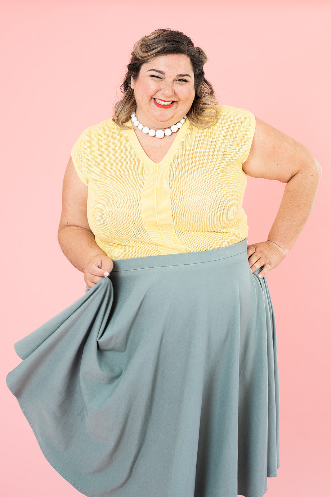 A plus-size white woman wearing a yellow top holds out the hem of her mint-coloured vintage-inspired skirt