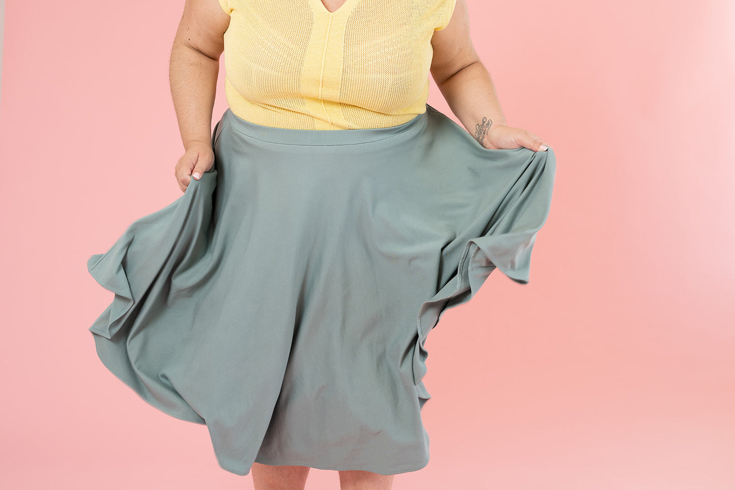 A woman wearing a light yellow top and a light blue skirt is swishing the hem of her skirt to show it off.