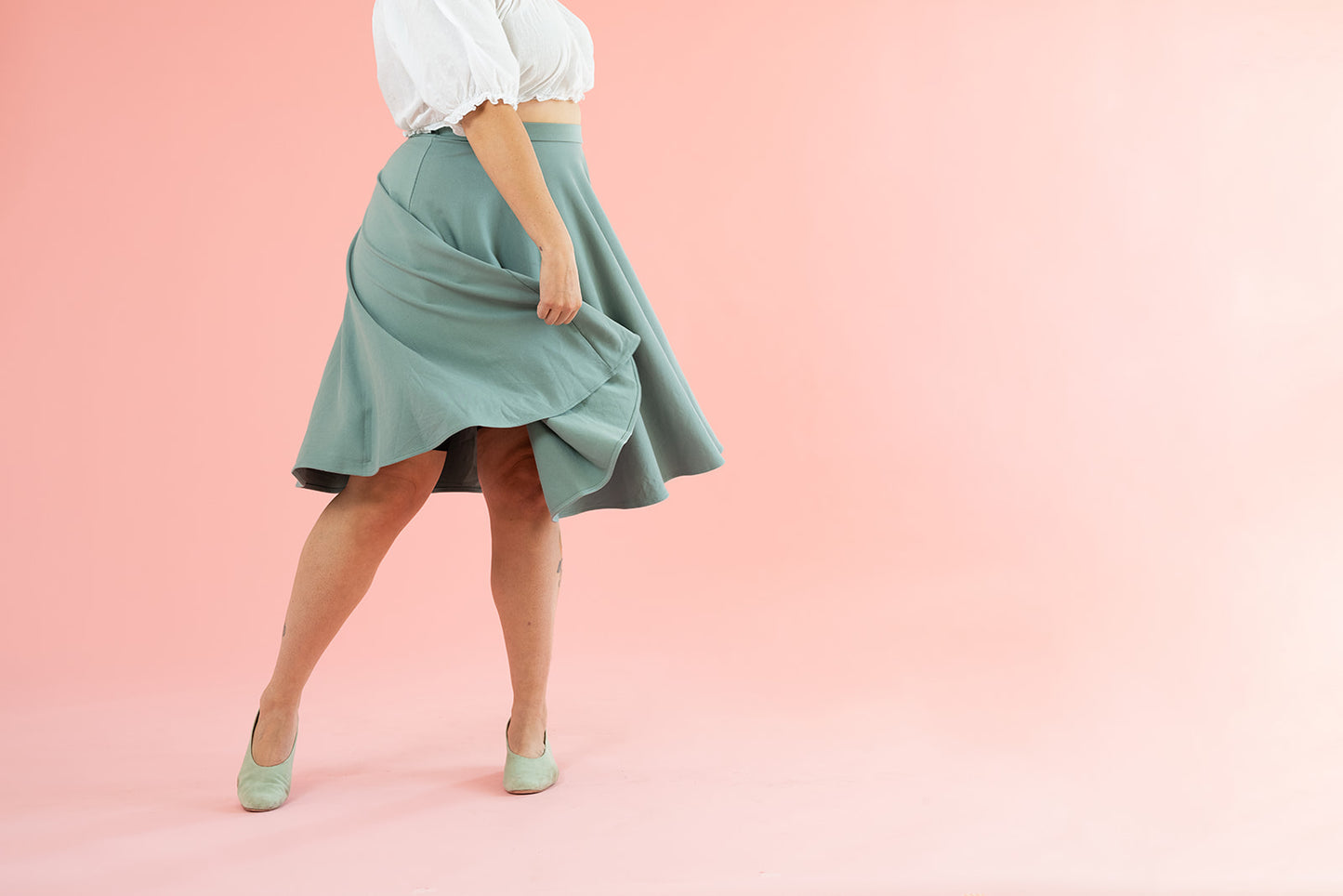 A woman in a white top twirls her flowy vintage-inspired mint skirt.