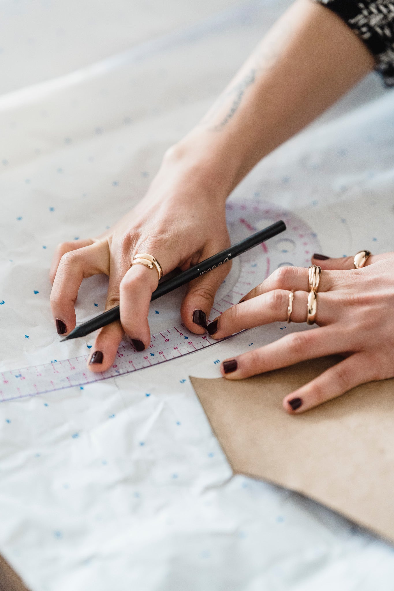 A person is using a french curve ruler to trace a pattern on paper for sewing a garment.